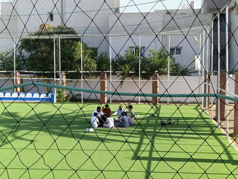A small study group sitting together outdoors on a green pitch